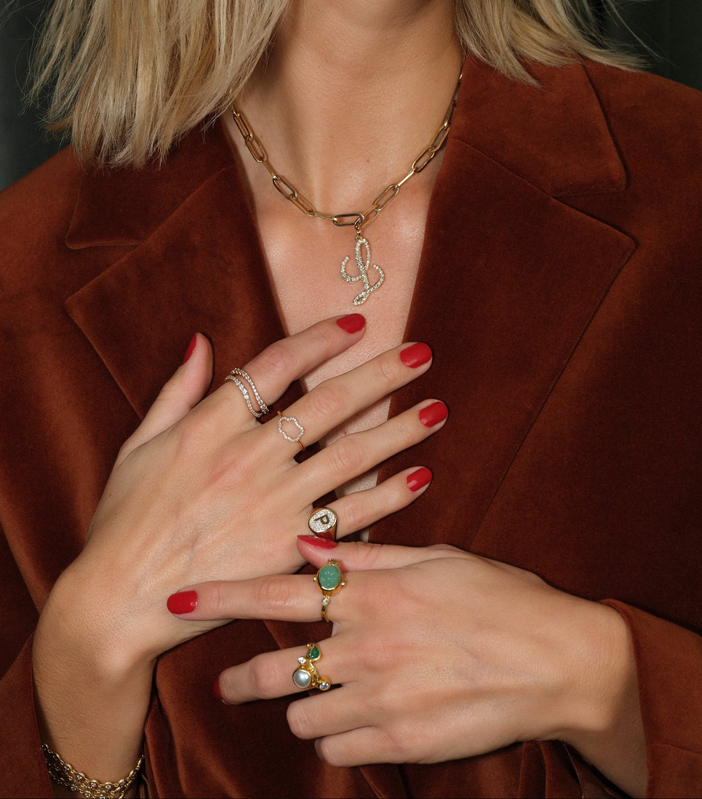 Person wearing a brown coat with visible jewelry on hands against a dark background